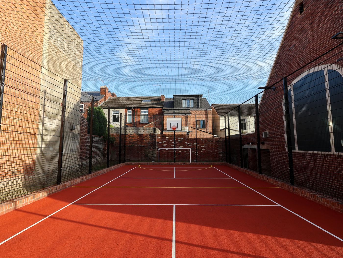 The netted outdoor games area with a red court, a goal and a basketball hoop
