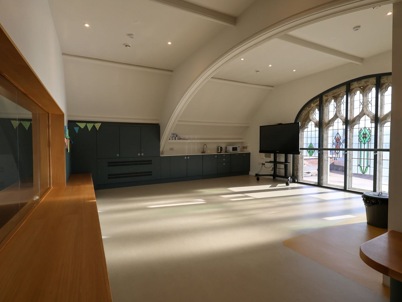 The new upstairs room, with sunlight through the arched stained-glass window, a kitchenette and a big screen